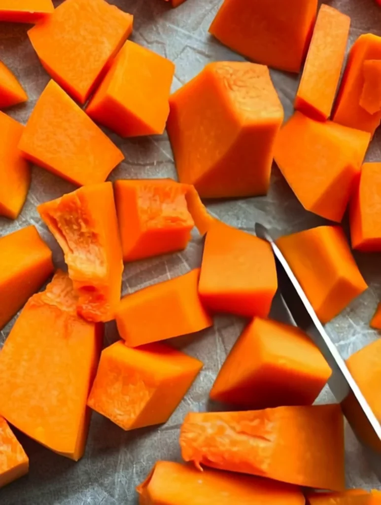 Freshly peeled and cubed pumpkin puree pieces arranged on a cutting board with a knife.