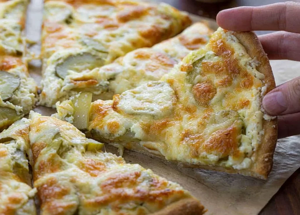 creamy baked pickle pizza with melted cheese and pickle slices being lifted from the pan – perfect for a pickle pizza recipe.
