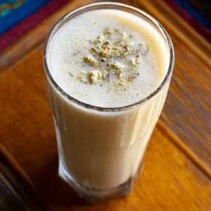 Banana chamomile tea smoothie in a glass with fresh banana and chamomile flowers.
