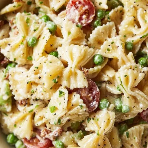 A bowl of creamy pasta salad with colorful vegetables and herbs.