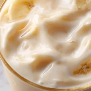 A glass of creamy Korean Banana Milk topped with a banana slice.